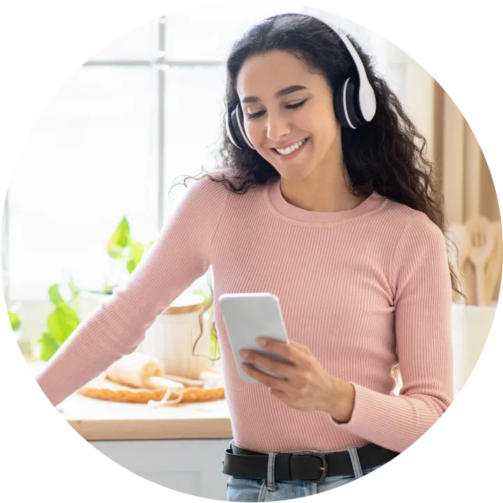 A woman wearing headphones and looking at a cell phone.